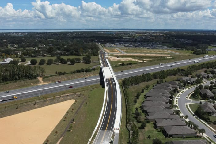New road construction with bridge over highway for site development projects, aerial view of infrastructure upgrade, rural residential area near water body, illustrating advanced site development techniques.