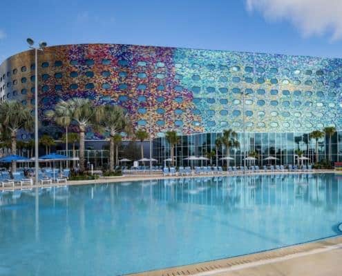 Colorful modern hotel building with poolside area, palm trees, and outdoor lounge chairs, showcasing innovative site development and contemporary architecture design.
