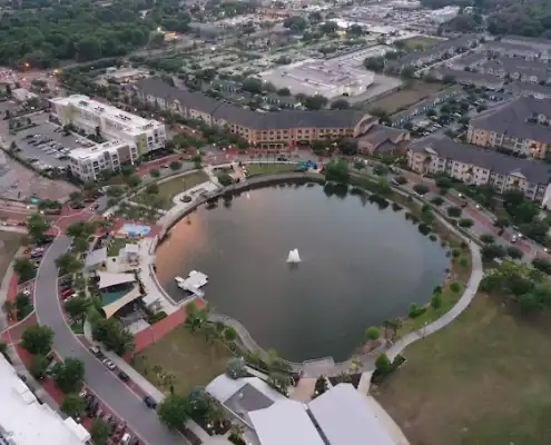 Colorful city park with pond, fountain, walking paths, and surrounding buildings showcasing urban development and landscaping in an aerial drone view.