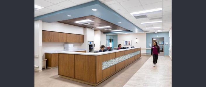 Modern hospital reception area with wood cabinetry and healthcare staff, emphasizing patient service and facility design.