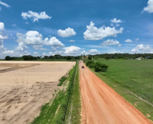 Spectacular aerial view of land development site showcasing dirt roads and open fields under a bright blue sky with fluffy clouds, emphasizing site infrastructure and progress.