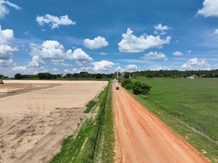Spectacular aerial view of land development site showcasing dirt roads and open fields under a bright blue sky with fluffy clouds, emphasizing site infrastructure and progress.