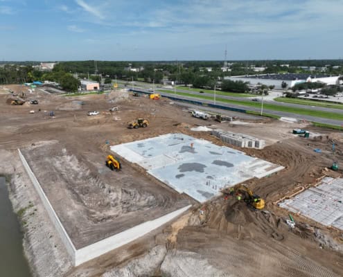 Excavation site for new commercial development with concrete foundation being poured, construction equipment, and materials on site.