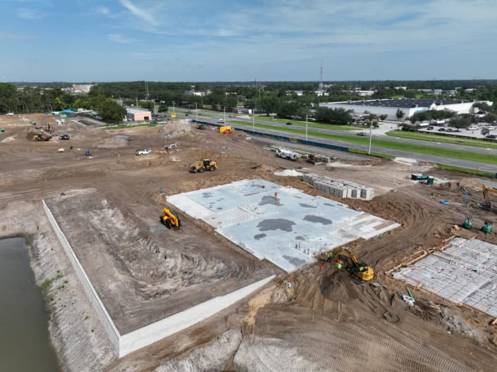 Excavation site for new commercial development with concrete foundation being poured, construction equipment, and materials on site.
