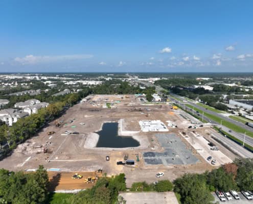 Excavation site for commercial development with building foundation in progress, water feature, and construction equipment on a large plot of land.