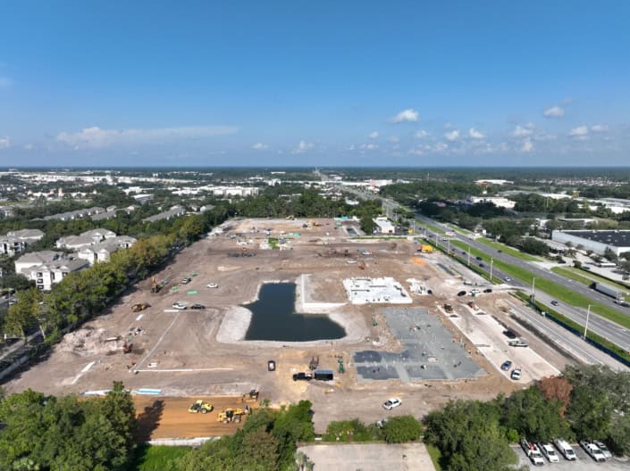 Excavation site for commercial development with building foundation in progress, water feature, and construction equipment on a large plot of land.