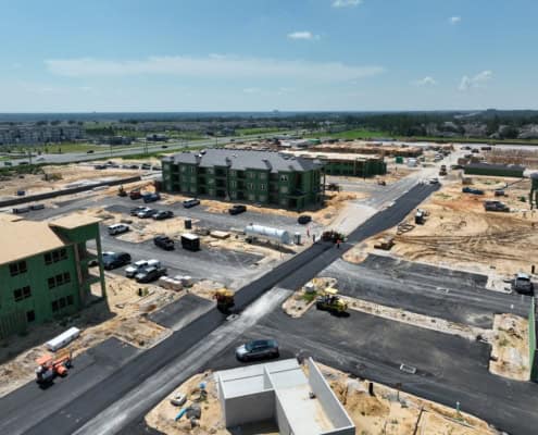 Modern new residential apartment complex construction site with green buildings in progress, heavy machinery, and paved roads.