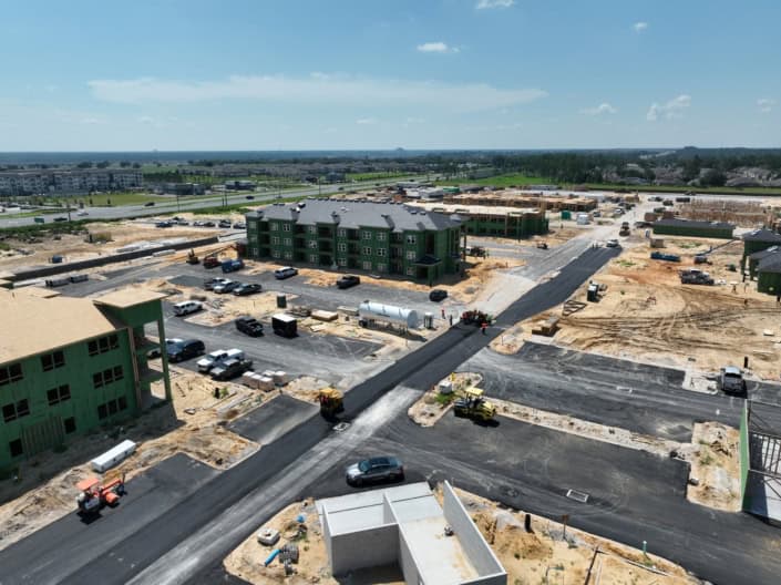 Modern new residential apartment complex construction site with green buildings in progress, heavy machinery, and paved roads.