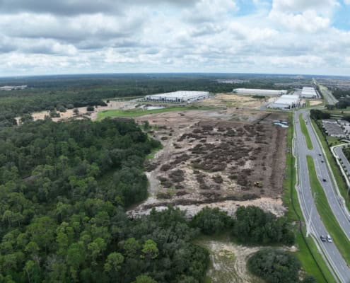 Modern industrial site development with ongoing construction and infrastructure expansion near wooded areas and major highways.