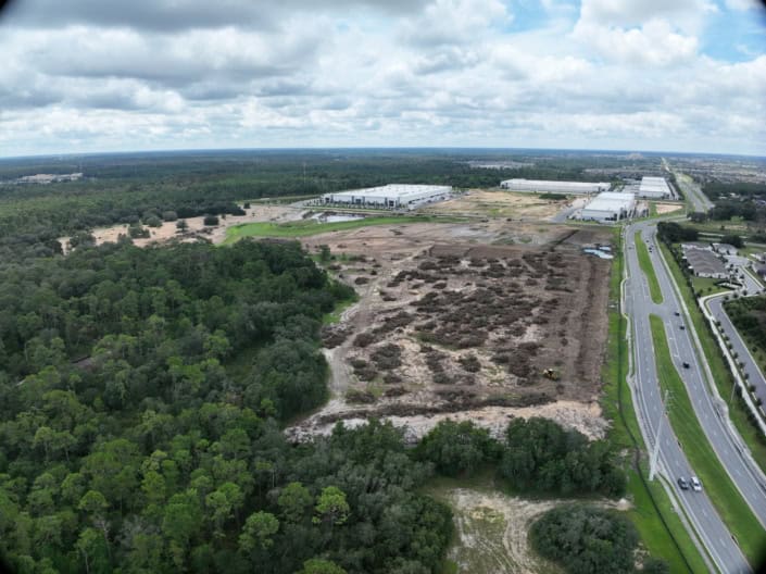 Modern industrial site development with ongoing construction and infrastructure expansion near wooded areas and major highways.