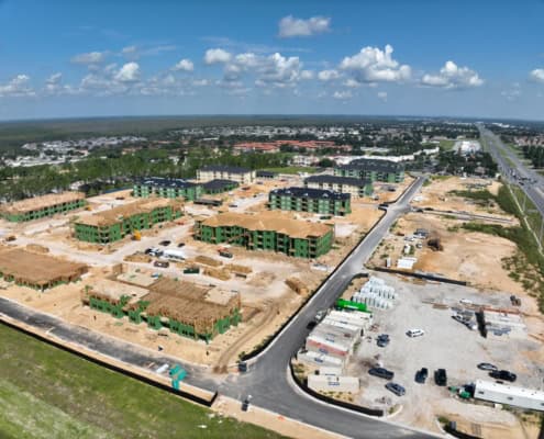 Multi-family residential construction site development with modern apartment complexes, ongoing building projects, and infrastructure improvements in a growing suburban area.