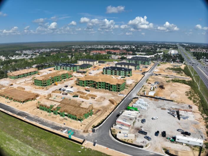 Multi-family residential construction site development with modern apartment complexes, ongoing building projects, and infrastructure improvements in a growing suburban area.