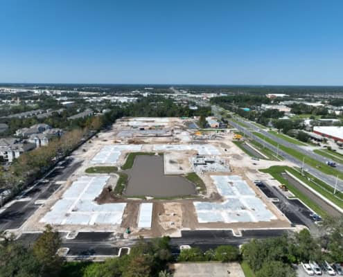 Wide aerial view of a commercial site under development with foundation work and construction equipment, showing progress on site development for retail or industrial space.