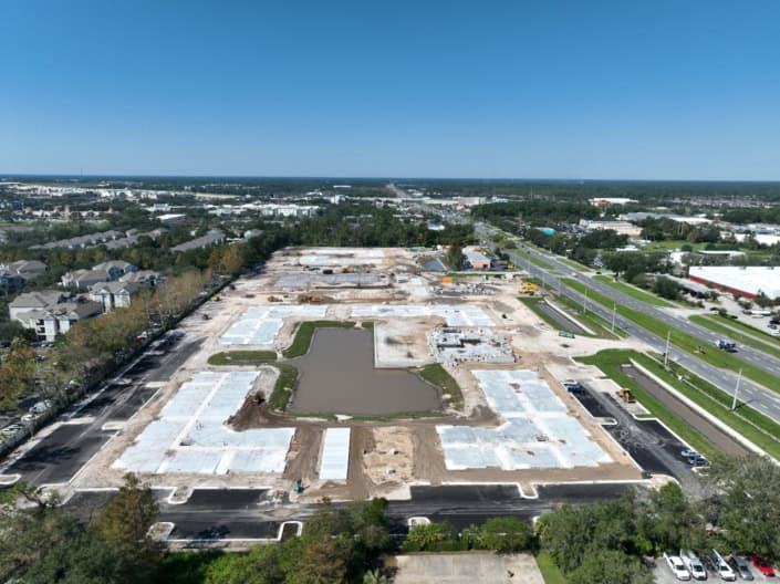 Wide aerial view of a commercial site under development with foundation work and construction equipment, showing progress on site development for retail or industrial space.