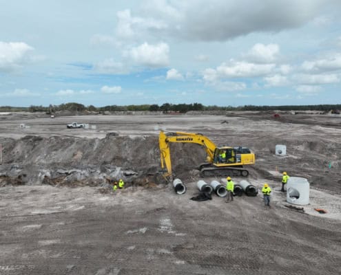 Excavation construction site for commercial development with heavy machinery and workers installing large concrete pipes, illustrating site development services.