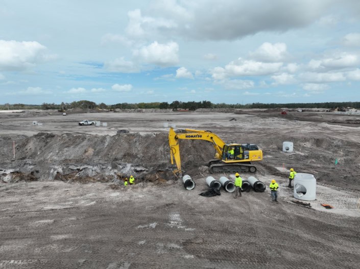 Excavation construction site for commercial development with heavy machinery and workers installing large concrete pipes, illustrating site development services.