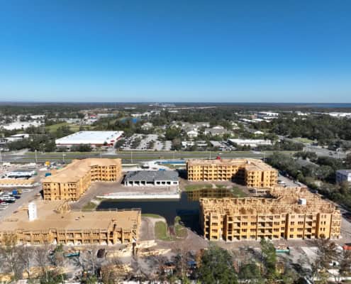 Modern multi-family residential construction site for apartment complex, showcasing wooden frameworks and ongoing building development, with surrounding commercial and green spaces.
