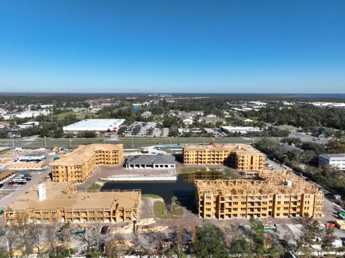 Modern multi-family residential construction site for apartment complex, showcasing wooden frameworks and ongoing building development, with surrounding commercial and green spaces.