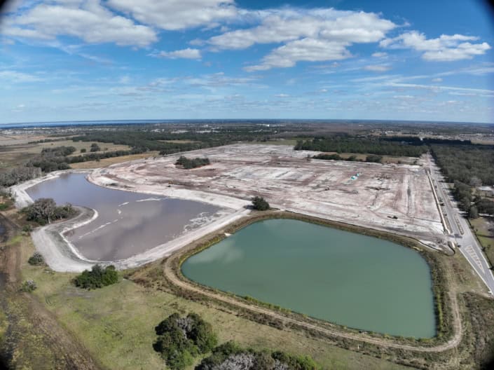 Aerial view of a site development project with ponds, construction area, and surrounding landscape, highlighting site planning, grading, and infrastructure development for commercial or residential purposes.