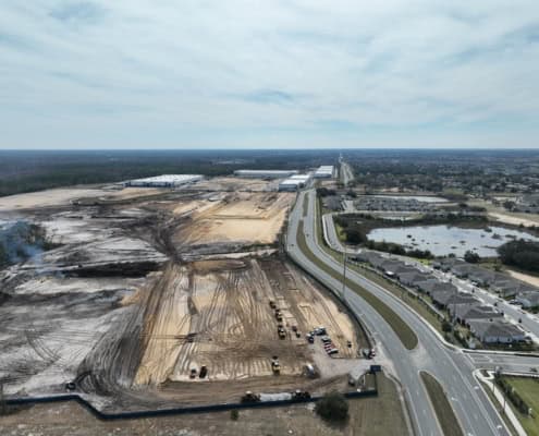 Excavation site for commercial and industrial development with construction vehicles, near residential neighborhoods and scenic water features, showcasing sustainable site development.