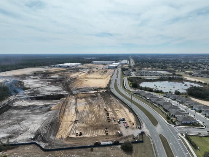 Excavation site for commercial and industrial development with construction vehicles, near residential neighborhoods and scenic water features, showcasing sustainable site development.