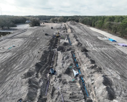 Excavation site for commercial development with heavy machinery and piping installation, demonstrating foundation work for new construction project.