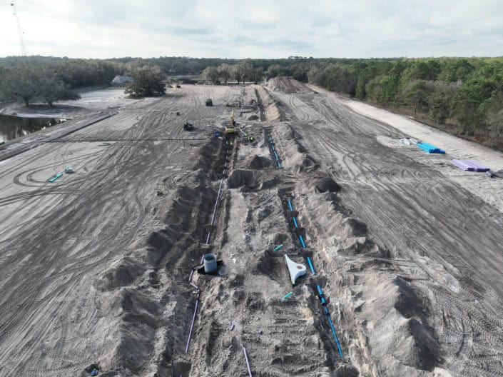 Excavation site for commercial development with heavy machinery and piping installation, demonstrating foundation work for new construction project.