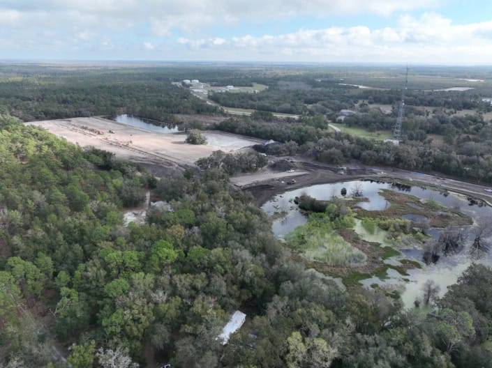 Aerial view of land development, construction site, and pond area surrounded by lush greenery, showcasing site preparation for commercial or industrial infrastructure development.