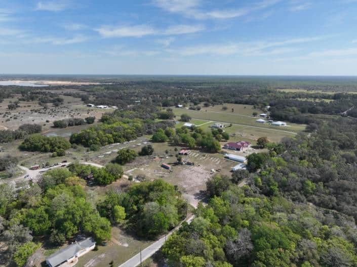 Vast rural land with green trees, open fields, and scattered buildings showcasing site development in Florida.
