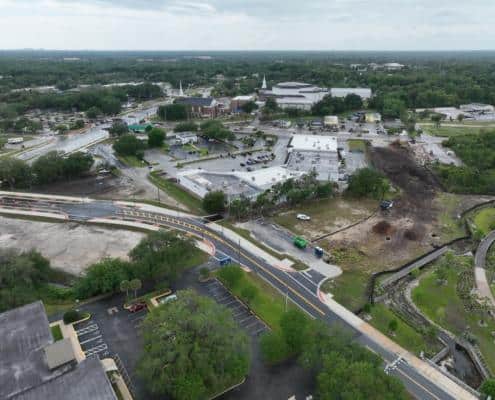 Aerial view of site development in progress with construction, landscaping, and infrastructure improvements in a bustling town area.
