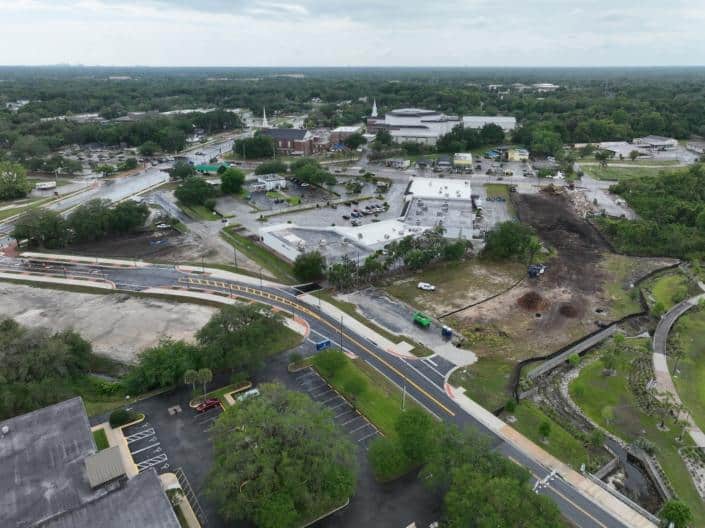 Aerial view of site development in progress with construction, landscaping, and infrastructure improvements in a bustling town area.