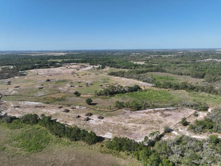 Aerial view of large undeveloped land for commercial or residential site development in Florida with open fields and trees.