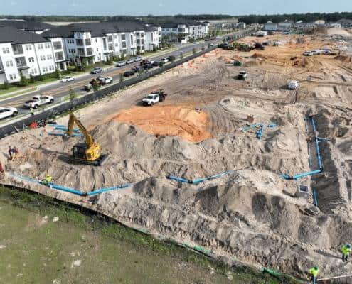 Excavation site for residential development with blue plumbing pipes, construction workers, and heavy machinery in a new housing project.