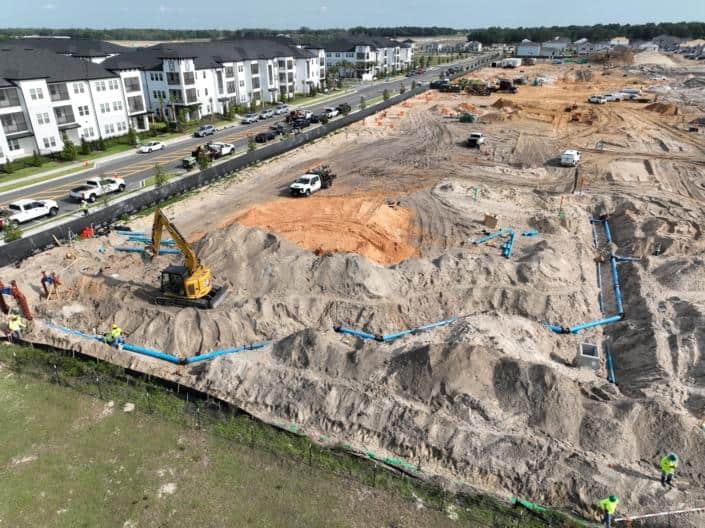 Excavation site for residential development with blue plumbing pipes, construction workers, and heavy machinery in a new housing project.