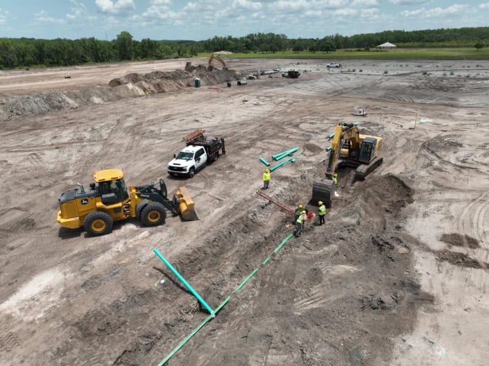 Heavy construction site with excavators, bulldozer, and workers installing utility pipes at a large development project.