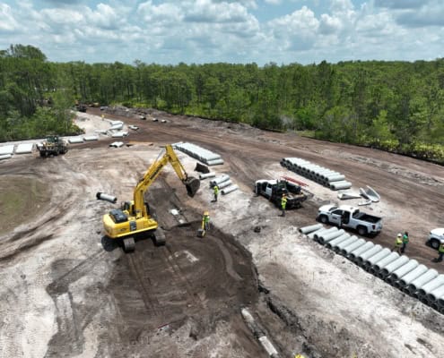 Heavy construction site with bulldozer laying groundwork for new infrastructure, piping and equipment installation, surrounded by trees and cloudy sky, focusing on site development services.