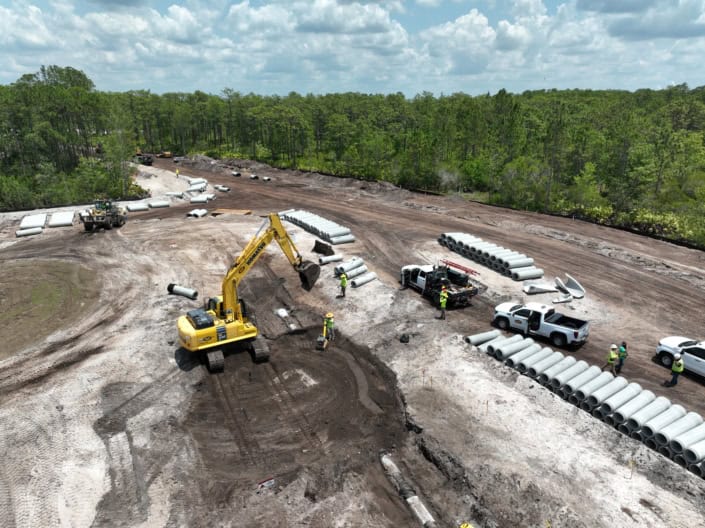 Heavy construction site with bulldozer laying groundwork for new infrastructure, piping and equipment installation, surrounded by trees and cloudy sky, focusing on site development services.