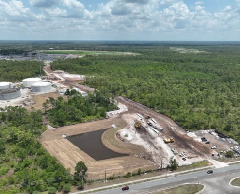 New construction site for industrial development with heavy earth-moving equipment and storage tanks.