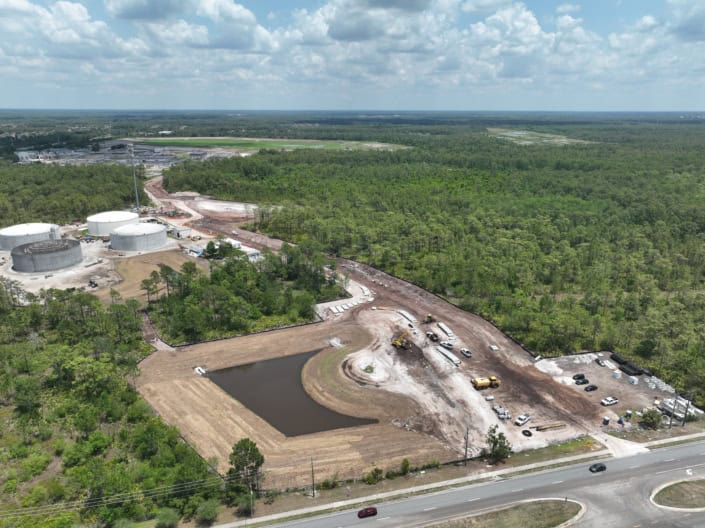 New construction site for industrial development with heavy earth-moving equipment and storage tanks.