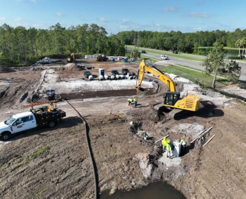 Excavation and site development for commercial construction with heavy machinery at a construction site by the highway, emphasizing groundwork and infrastructure setup.