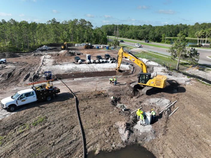 Excavation and site development for commercial construction with heavy machinery at a construction site by the highway, emphasizing groundwork and infrastructure setup.