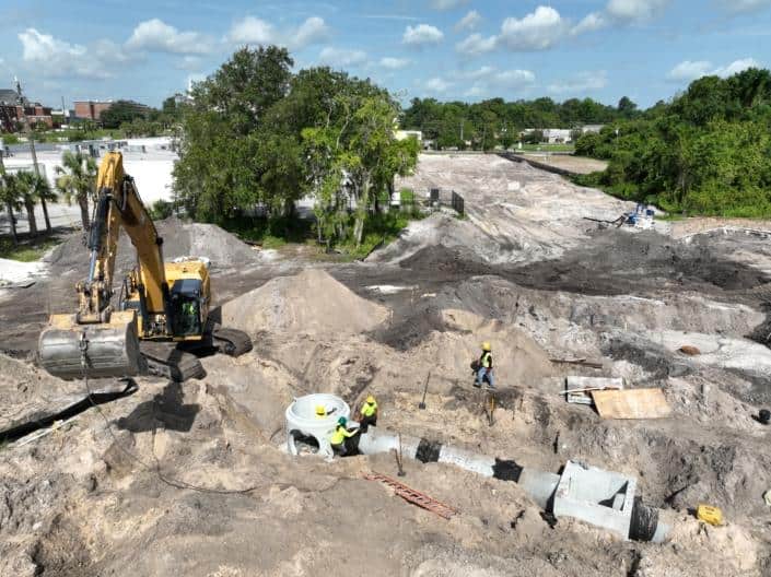Heavy construction site with excavator and workers installing underground utilities, preparing the land for development, showcasing site development services.