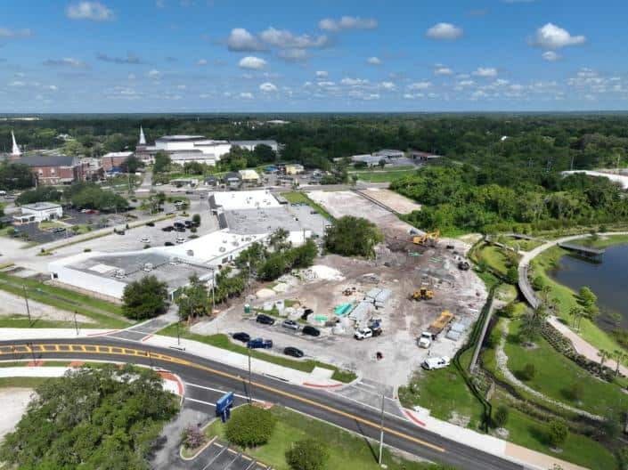 Construction site progress for commercial development project overlooking landscaped park and parking lot.