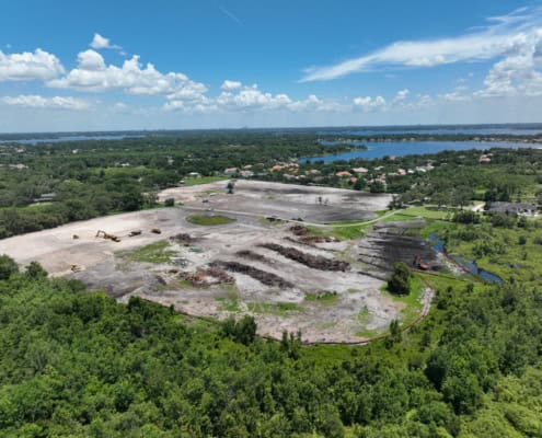 Open land development site with construction machinery, cleared land, and surrounding greenery, ready for commercial or residential development, showcasing professional site development services.