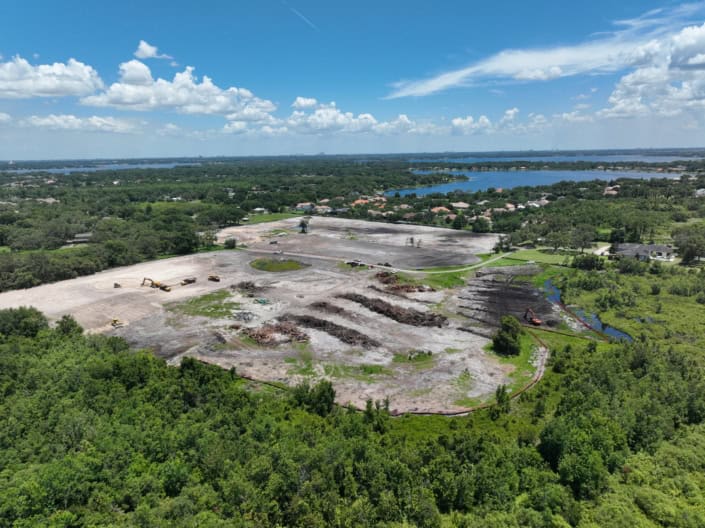 Open land development site with construction machinery, cleared land, and surrounding greenery, ready for commercial or residential development, showcasing professional site development services.