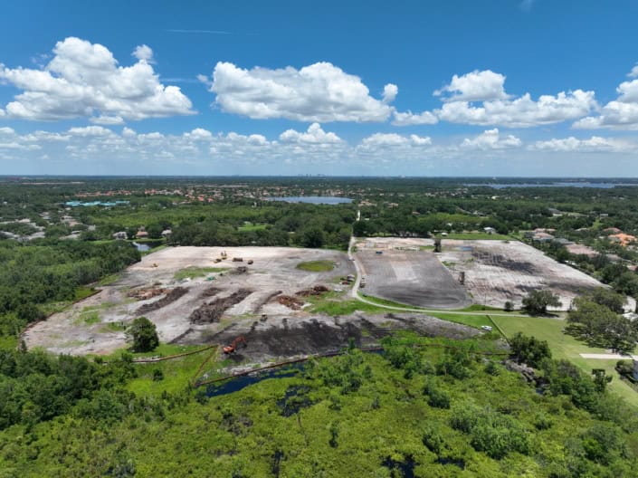 Aerial view of site development with cleared land, construction equipment, and surrounding greenery for commercial or residential real estate projects.