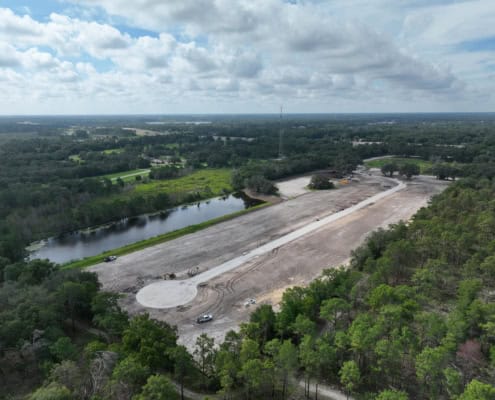 Aerial view of land development site for construction, surrounded by lush greenery, with ongoing grading work and a pond, emphasizing site development services and infrastructure planning.