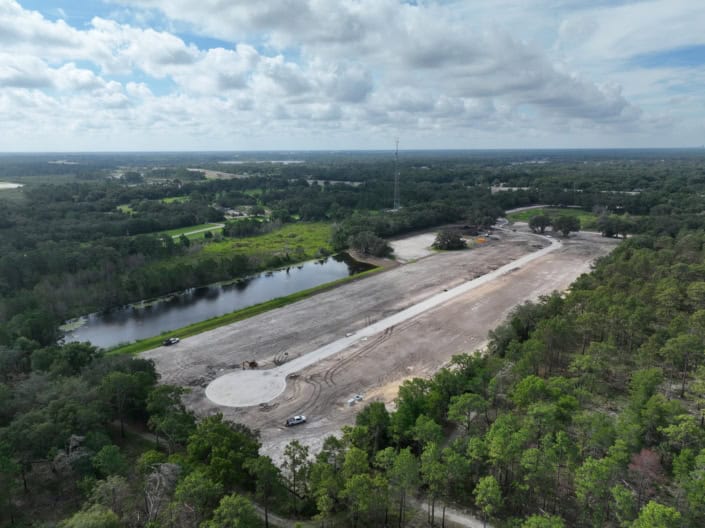 Aerial view of land development site for construction, surrounded by lush greenery, with ongoing grading work and a pond, emphasizing site development services and infrastructure planning.