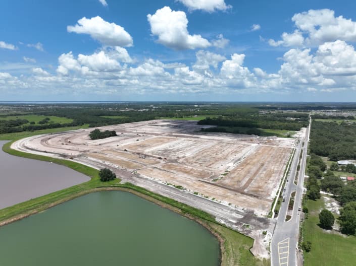 Large commercial site development with extensive land clearing and lot layout, adjacent to water bodies, under construction for future industrial or business use.