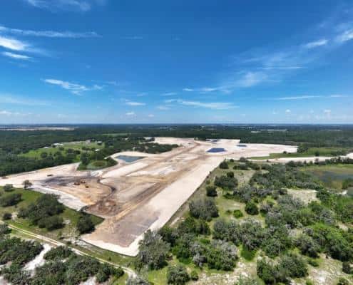 Aerial view of site development for commercial or industrial construction with land clearing, grading, and water features.